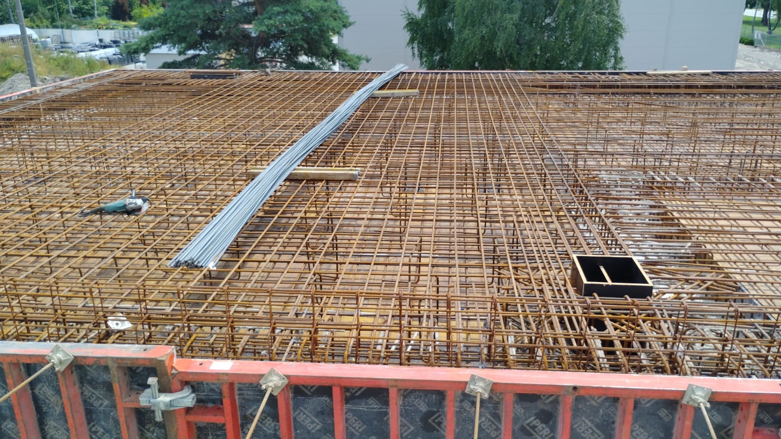 Zbrojenie stropu z widocznym szlifierką kątową i formami szalunkowymi PERI, przygotowane do zalania betonem. Widok z góry na plac budowy.
