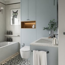 Michał Wilkosiński Conifer Media - Jasna łazienka w szaro-błękitnych tonach z wanną, toaletą i umywalką. Na ścianie grafika kota w okularach. Na podłodze wzorzyste płytki. Nowoczesny design.