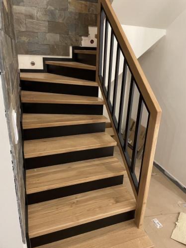 Nowoczesne schody z drewnianymi stopniami i czarną podstopnicą oraz metalową balustradą z drewnianym pochwytem, widok z dołu.