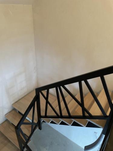 Jasne, drewniane schody z czarną, geometryczną balustradą, widziane z góry. Minimalistyczny design, naturalne światło, kremowe ściany w tle.