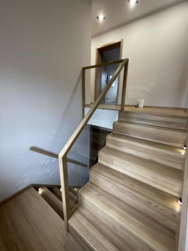 Jasne schody z drewna z podświetleniem i szklaną balustradą, widok z dołu. Minimalistyczny design, ciepłe oświetlenie punktowe.