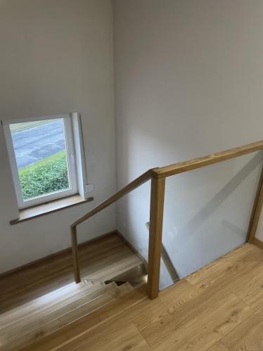 Jasne schody z drewna i szkła w nowoczesnym domu, oświetlone światłem z okna. Minimalistyczny design, widok z góry na stopnie i balustradę.