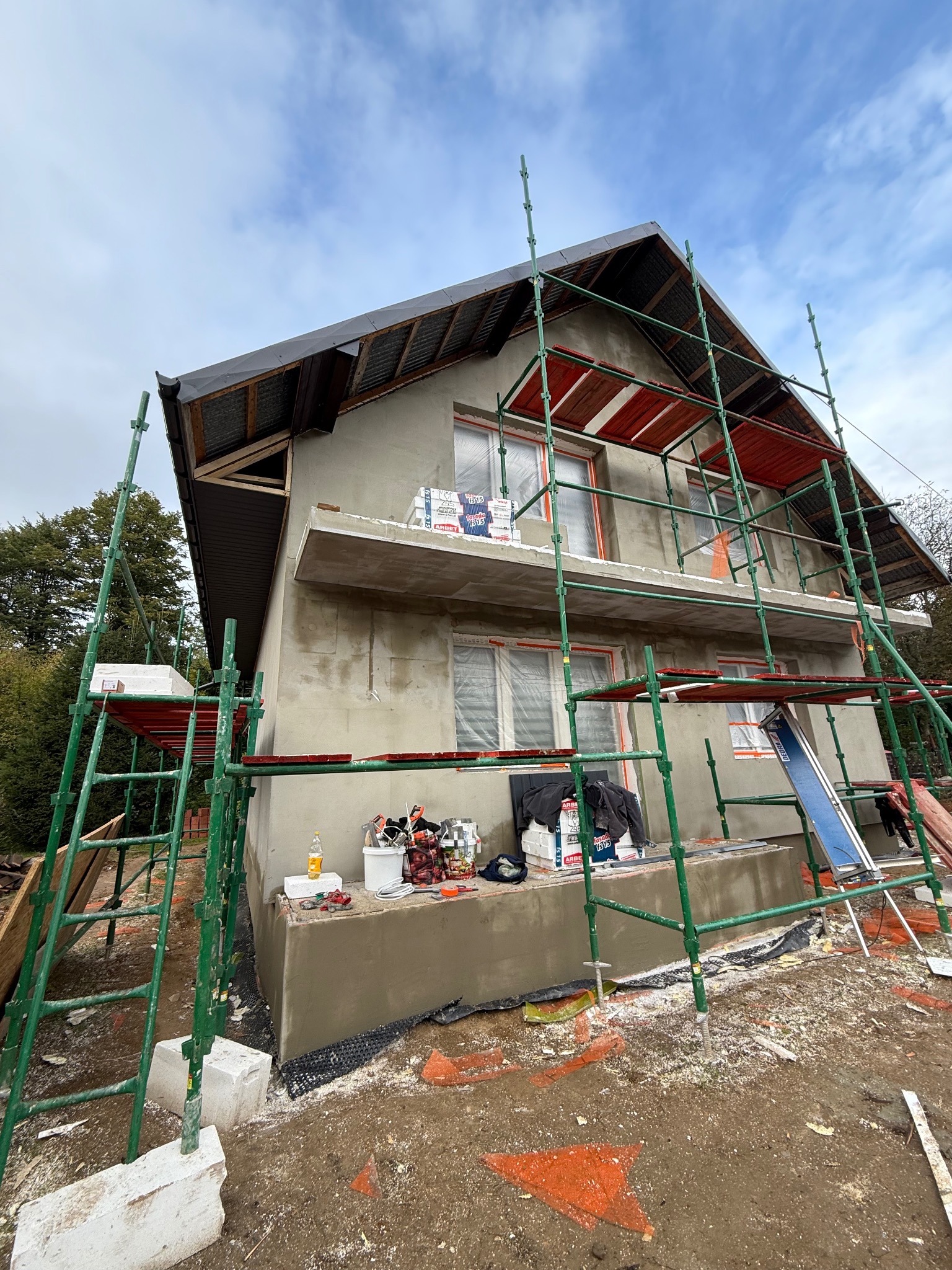 Dom jednorodzinny w trakcie ocieplania elewacji, widoczne rusztowania, materiały budowlane i narzędzia. Ujęcie z dołu, podkreślające wysokość budynku.