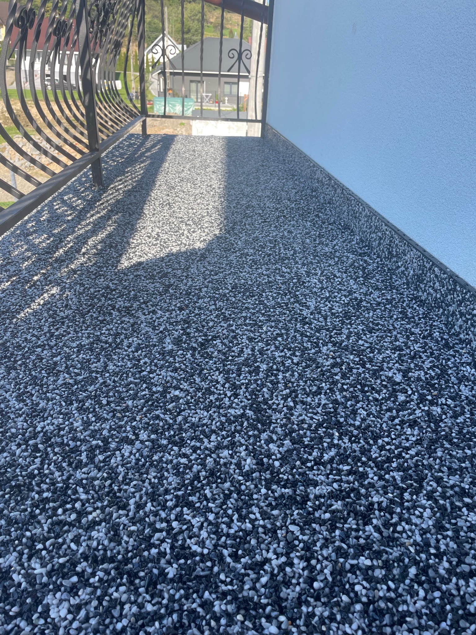 Balkon z posadzką z żywicy epoksydowej w odcieniach szarości, z widoczną metalową balustradą i fragmentem elewacji w tle. Nowoczesne wykończenie balkonu.