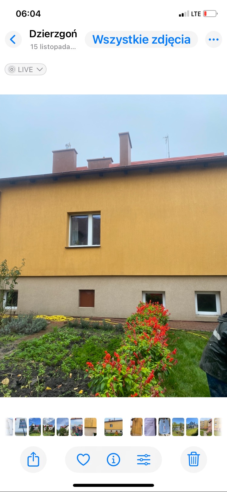 Dwukondygnacyjny budynek z żółtą elewacją i brązowymi kominami. Widoczne okna, roślinność i fragment osoby. Ujęcie z dołu, pochmurna pogoda.