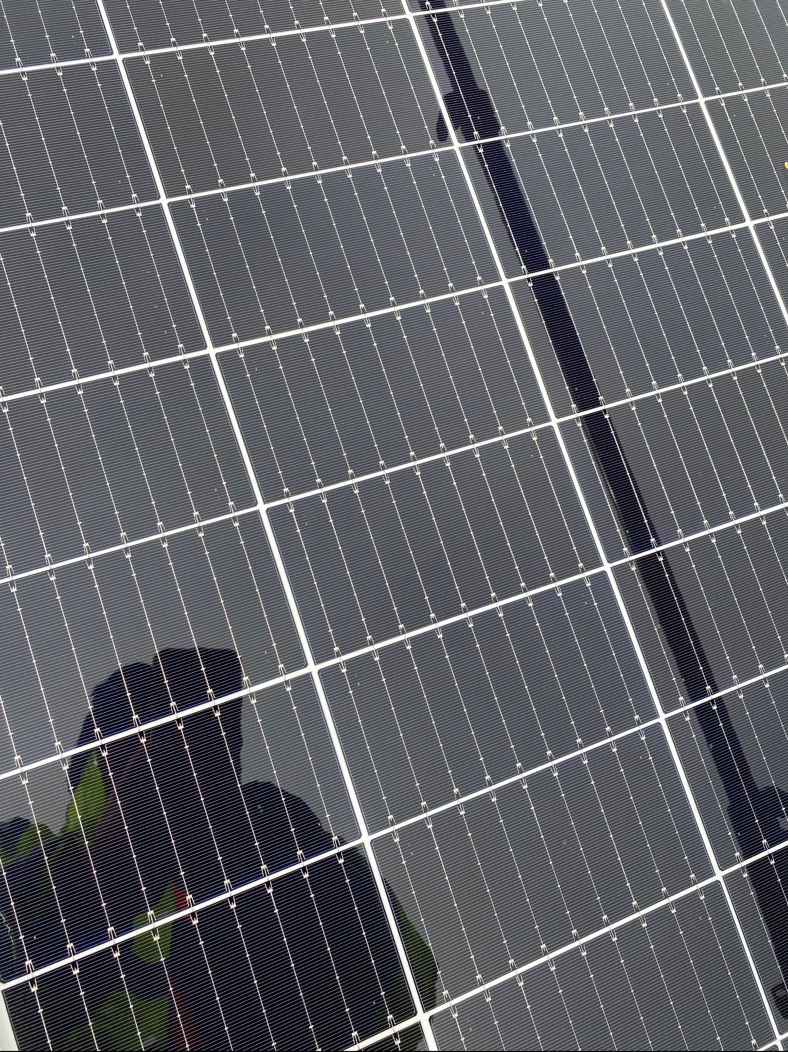 Błyszczące panele słoneczne z odbiciem osoby w odzieży roboczej. Widoczne regularne podziały paneli i drobne detale konstrukcyjne.