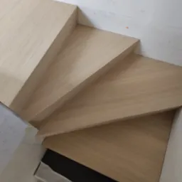 Jasne, drewniane stopnie schodów w trakcie montażu, widoczne zabezpieczenia podłoża, ujęcie z góry.