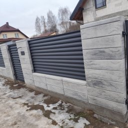 Usługi budowlane Arkadiusz komar - Nowoczesne ogrodzenie panelowe z betonowymi słupkami i poziomymi, grafitowymi przęsłami, częściowo pokryte śniegiem, na tle budowy domu.