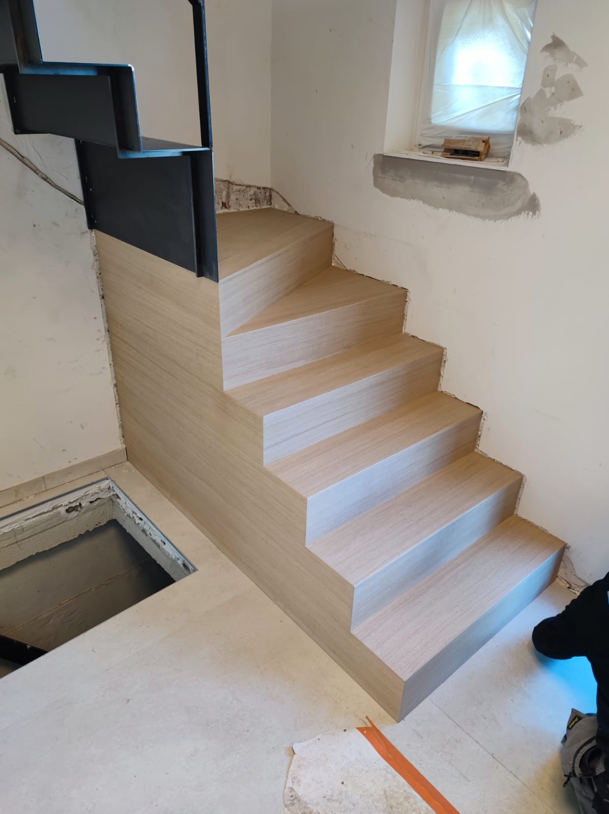 Montaż schodów drewnianych z metalową barierką w Daniłowie Małym. Jasne drewno, minimalistyczny design, widoczne niedokończone wykończenia ścian.