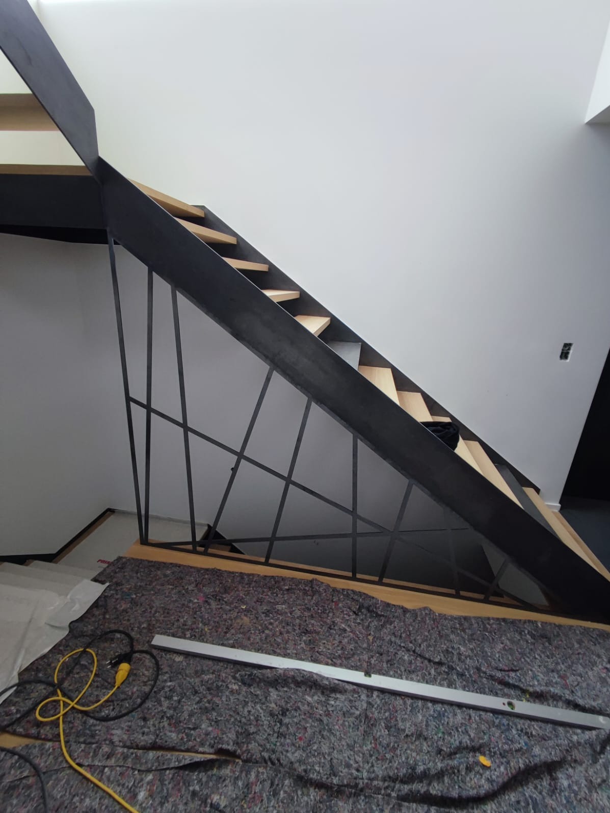 Nowoczesne schody drewniane z metalową konstrukcją, zabezpieczone podczas montażu, z widoczną poziomicą i kablem zasilającym.