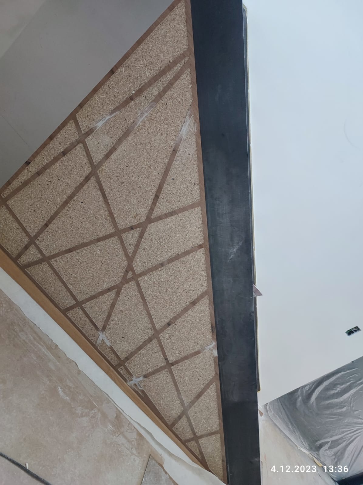 Montaż sufitu z płyty OSB z dekoracyjnymi listwami i widocznymi punktami mocowania. Fragment ściany i sufitu w tle. Ujęcie z dołu podkreśla perspektywę.