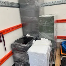 Sprzęt AGD (lodówka Siemens, pralka, płyta indukcyjna Amica) zabezpieczony folią stretch, gotowy do transportu wewnątrz przestrzeni ładunkowej. Widoczne elementy mocujące.