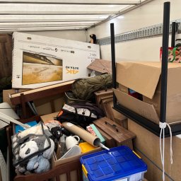 M&S-TRANSPORT SPÓŁKA Z OGRANICZONĄ ODPOWIEDZIALNOŚCIĄ - Wnętrze furgonetki załadowane różnorodnymi przedmiotami podczas przeprowadzki, w tym pudełko z telewizorem 4K, meble, torby i inne rzeczy osobiste, zabezpieczone sznurkami.