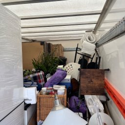 M&S-TRANSPORT SPÓŁKA Z OGRANICZONĄ ODPOWIEDZIALNOŚCIĄ - Wnętrze furgonetki wypełnionej różnorodnymi przedmiotami, w tym meblami, roślinami i pudełkami, przygotowanymi do transportu. Widoczny fragment lampy i krzesła.