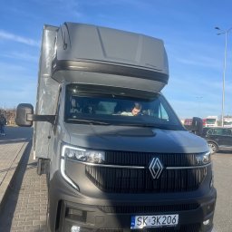 M&S-TRANSPORT SPÓŁKA Z OGRANICZONĄ ODPOWIEDZIALNOŚCIĄ - Nowoczesny, szary van Renault z zabudową Carpol, z charakterystycznymi LED-owymi światłami, zaparkowany na brukowanym parkingu w słoneczny dzień. W kabinie widoczny kierowca.