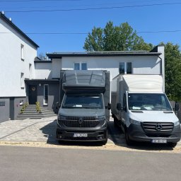 M&S-TRANSPORT SPÓŁKA Z OGRANICZONĄ ODPOWIEDZIALNOŚCIĄ - Dwa busy dostawcze, szary Renault i biały Mercedes Sprinter, zaparkowane na podjeździe z kostki brukowej przed nowoczesnym, dwupiętrowym domem w słoneczny dzień.