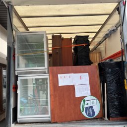 M&S-TRANSPORT SPÓŁKA Z OGRANICZONĄ ODPOWIEDZIALNOŚCIĄ - Wnętrze otwartej ciężarówki: zabezpieczone pasami meble, dwie białe lodówki wystawowe, przedmioty w czarnych workach; na meblu naklejka Apteline.