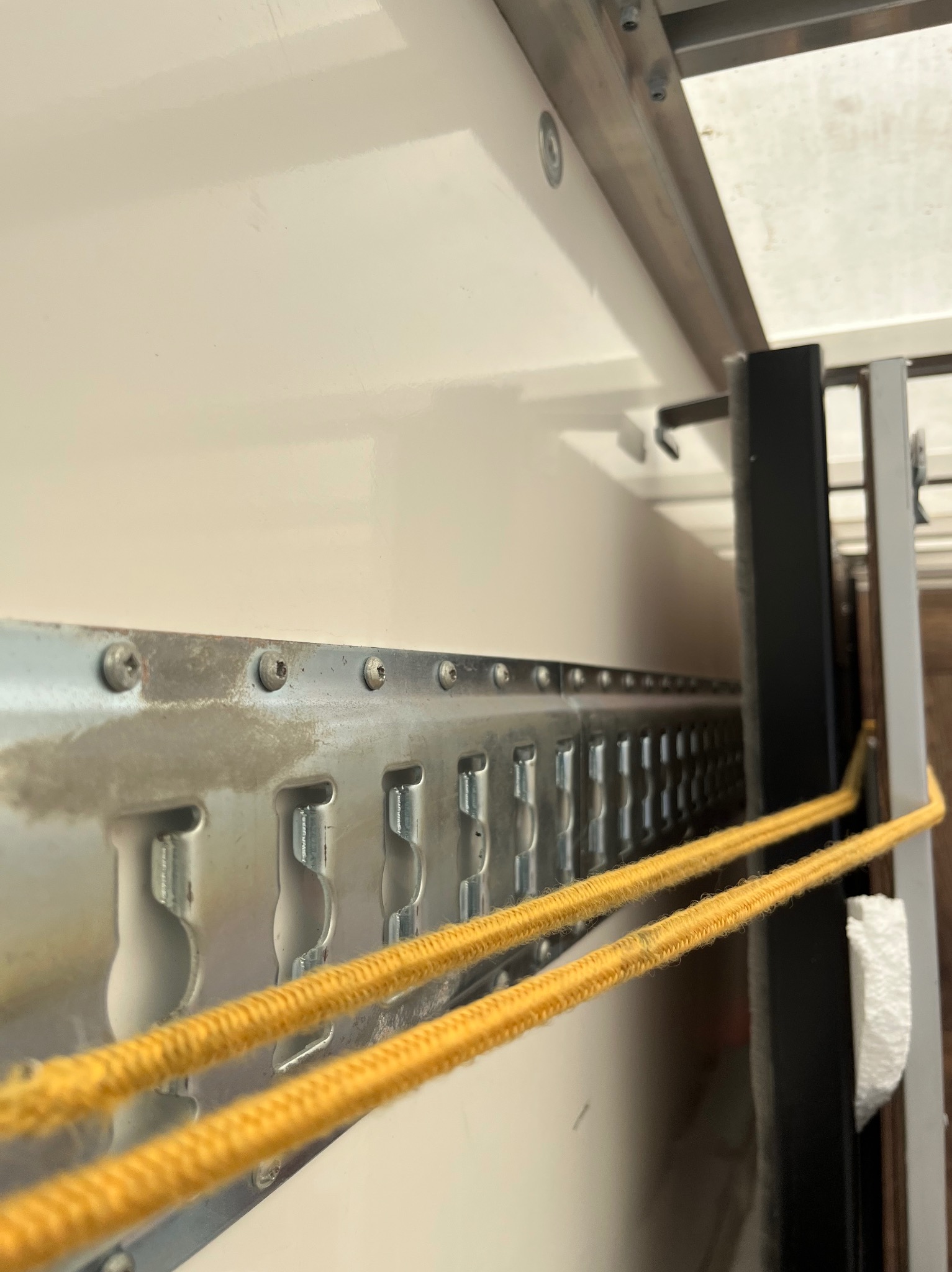 Wnętrze pojazdu transportowego z szyną mocującą ładunek i żółtymi linami zabezpieczającymi, ustawione pod kątem.