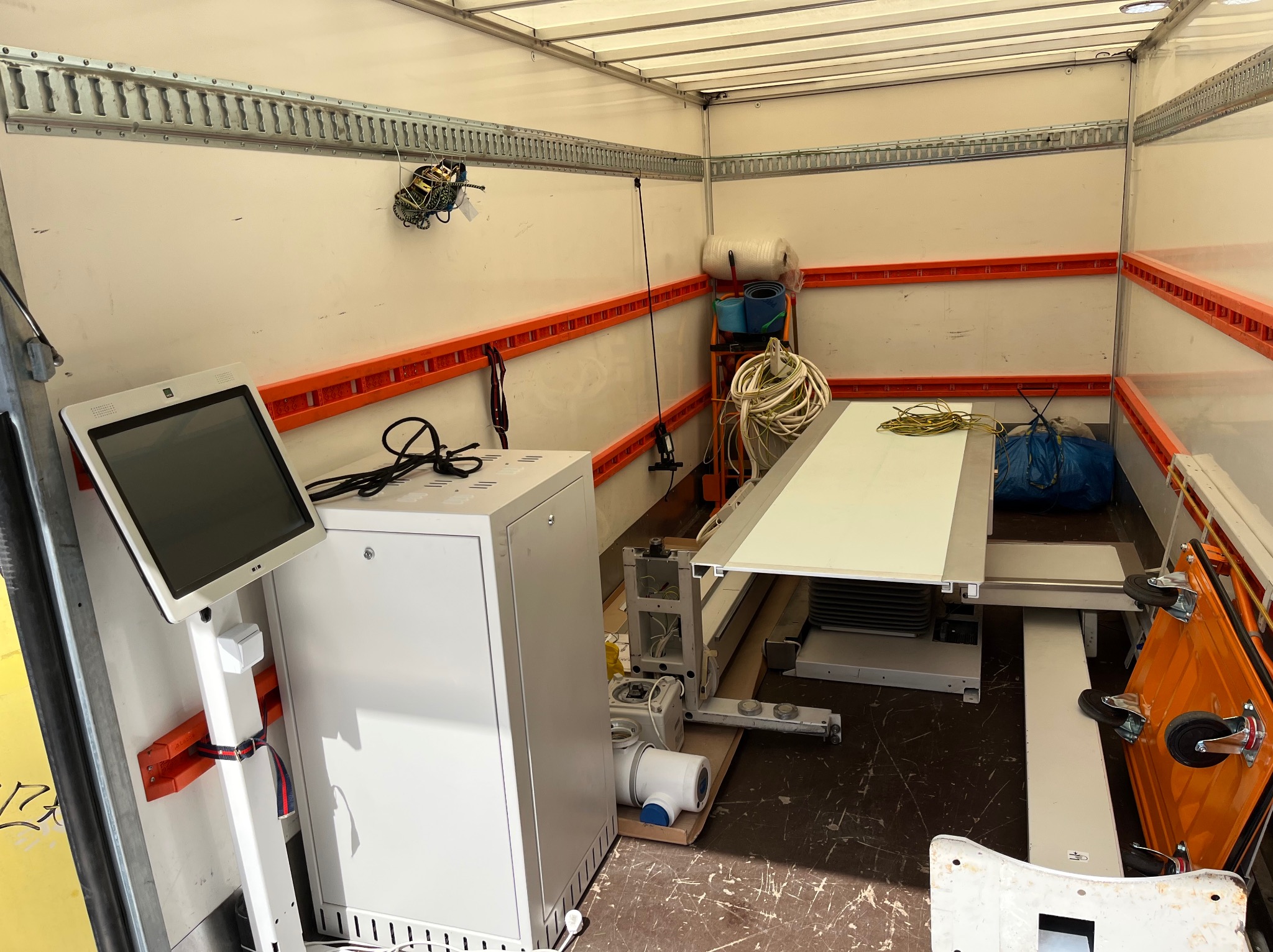 Wnętrze furgonetki z systemem mocowań, przewożącej specjalistyczny sprzęt medyczny: białą szafę z monitorem, przewody, wózek transportowy i inne akcesoria.