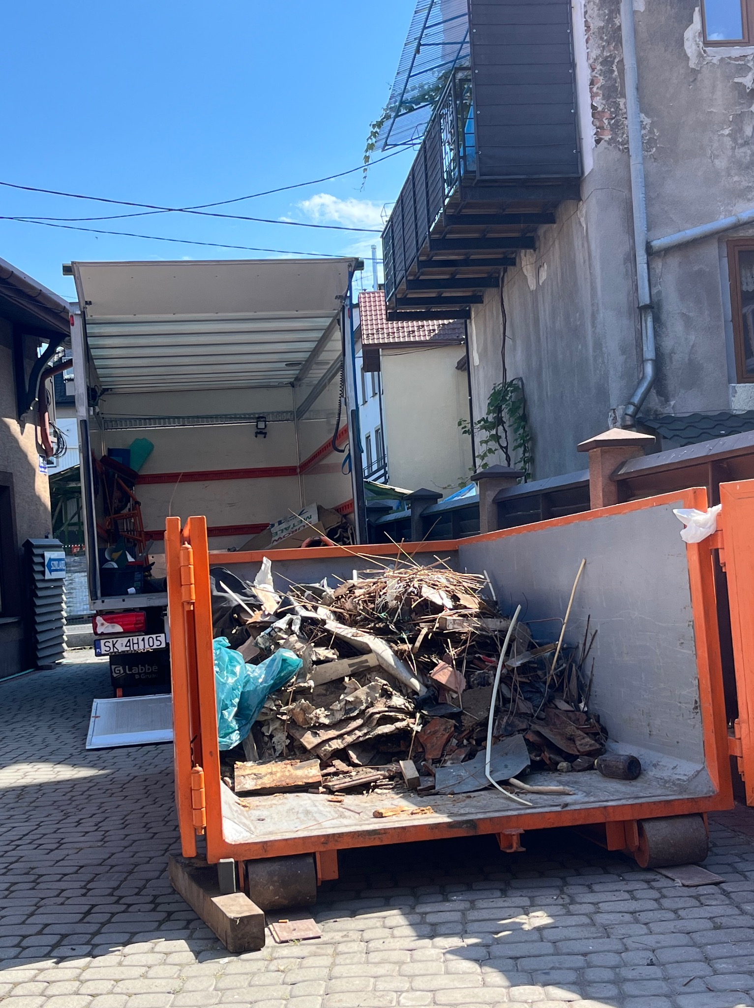 Kontener z gruzem i transport busem w tle, Hanusek. Wywóz odpadów budowlanych po remoncie. Widoczne elementy konstrukcyjne i resztki materiałów.