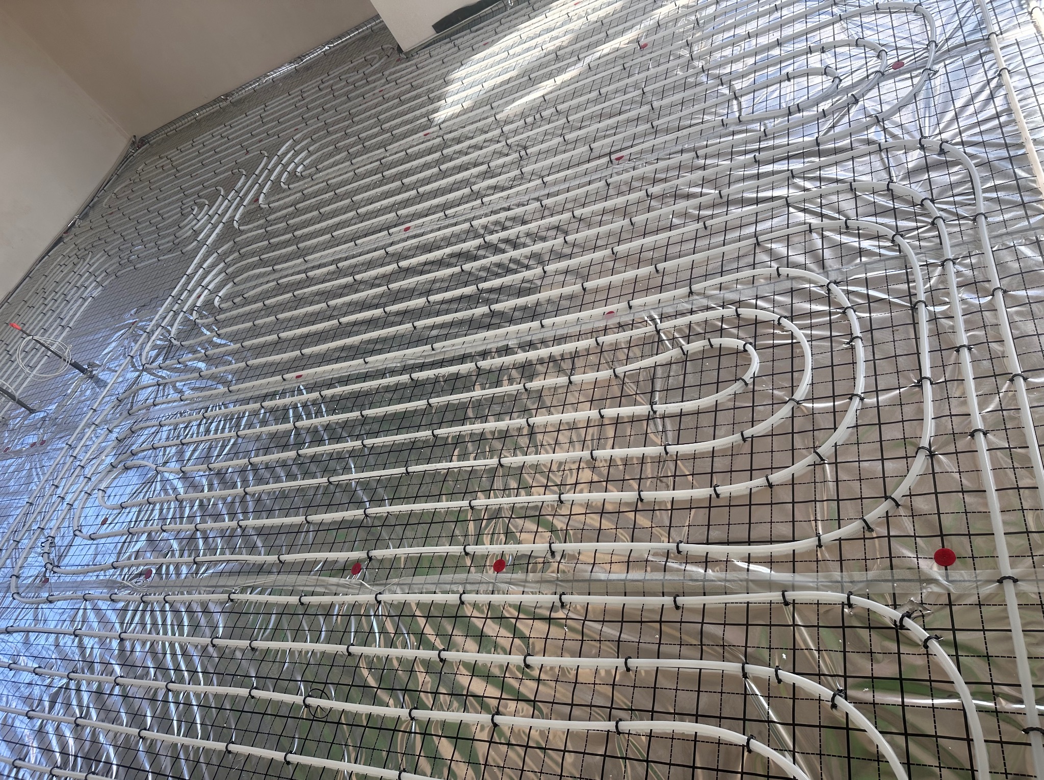 Białe rury ogrzewania podłogowego ułożone na srebrnej folii i siatce w Gorzowie Wielkopolskim, widok z góry. Instalacja przed wylaniem posadzki.