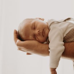 Inner Light - Fotografia Ślubna - Delikatne ujęcie śpiącego noworodka, trzymanego w dłoniach dorosłego. Jasna tonacja, miękkie światło podkreśla niewinność dziecka.