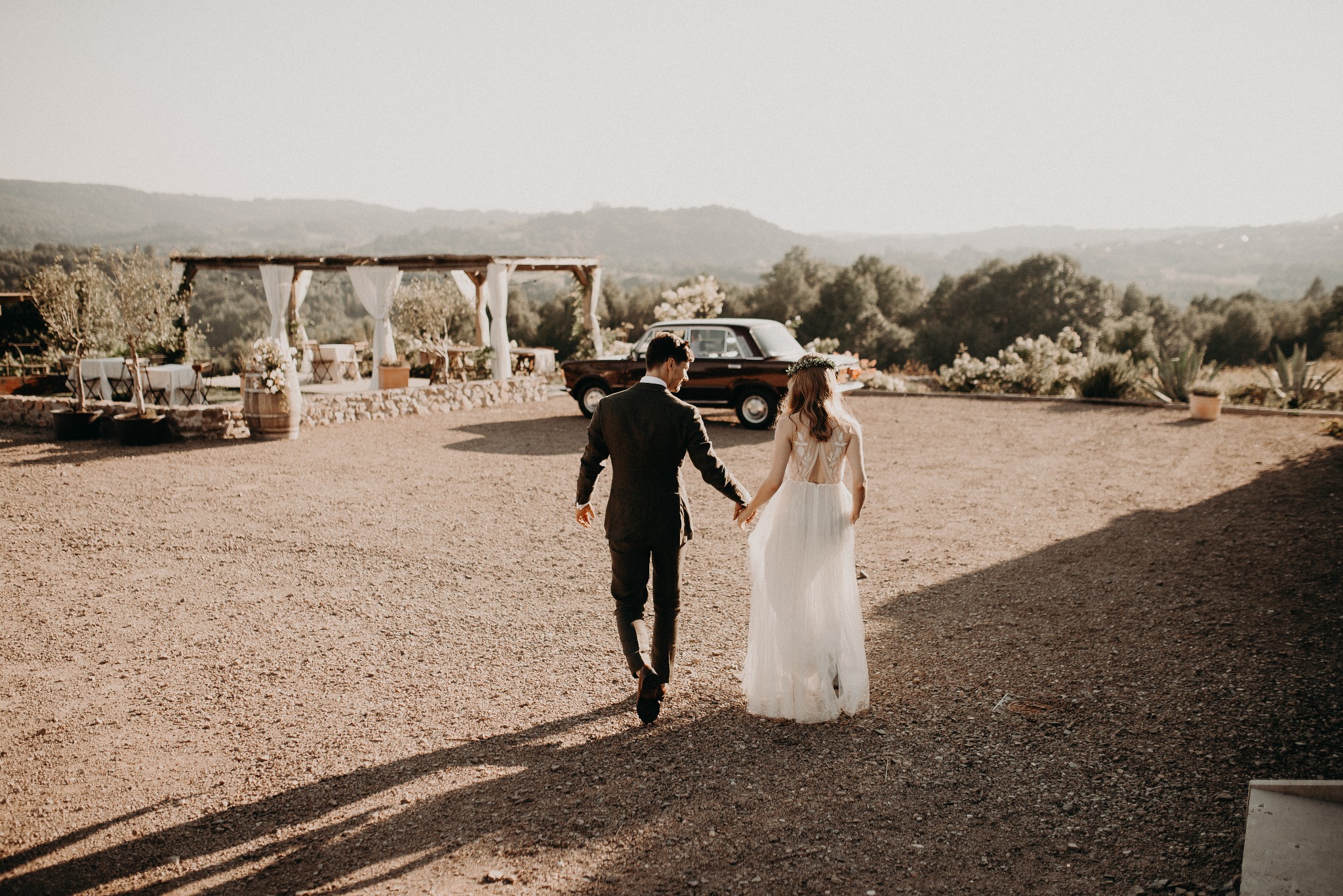 Para młoda, trzymając się za ręce, idzie w stronę zabytkowego auta w plenerze. Romantyczna sceneria ślubna w Gliwicach.
