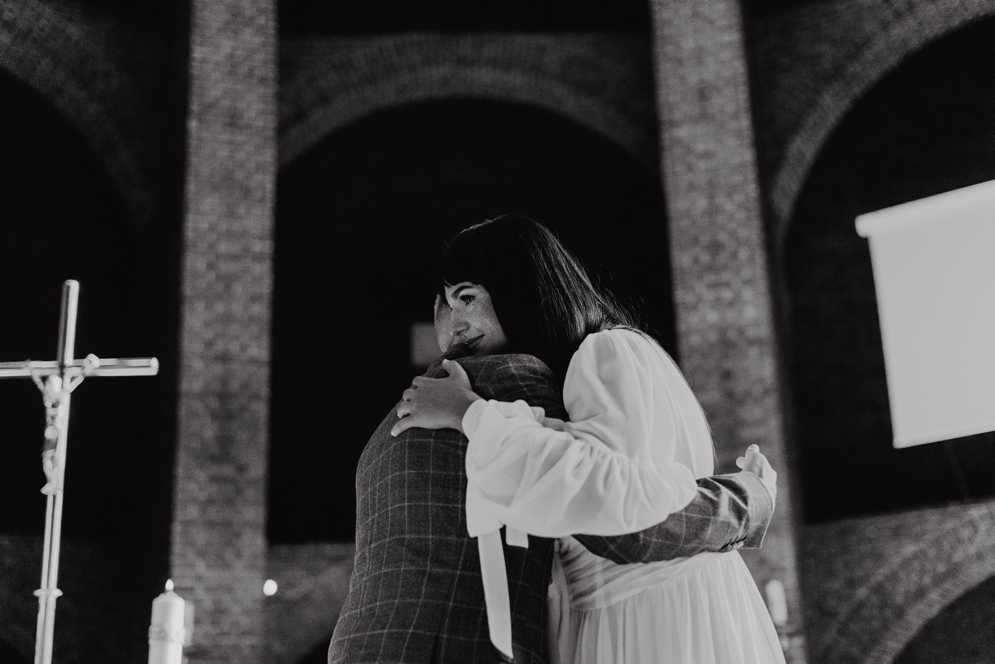 Czarno-białe zdjęcie z Gliwic: para młoda obejmująca się w kościele, widoczny krucyfiks i ceglane ściany w tle. Ujęcie z dołu podkreśla sakralny charakter.