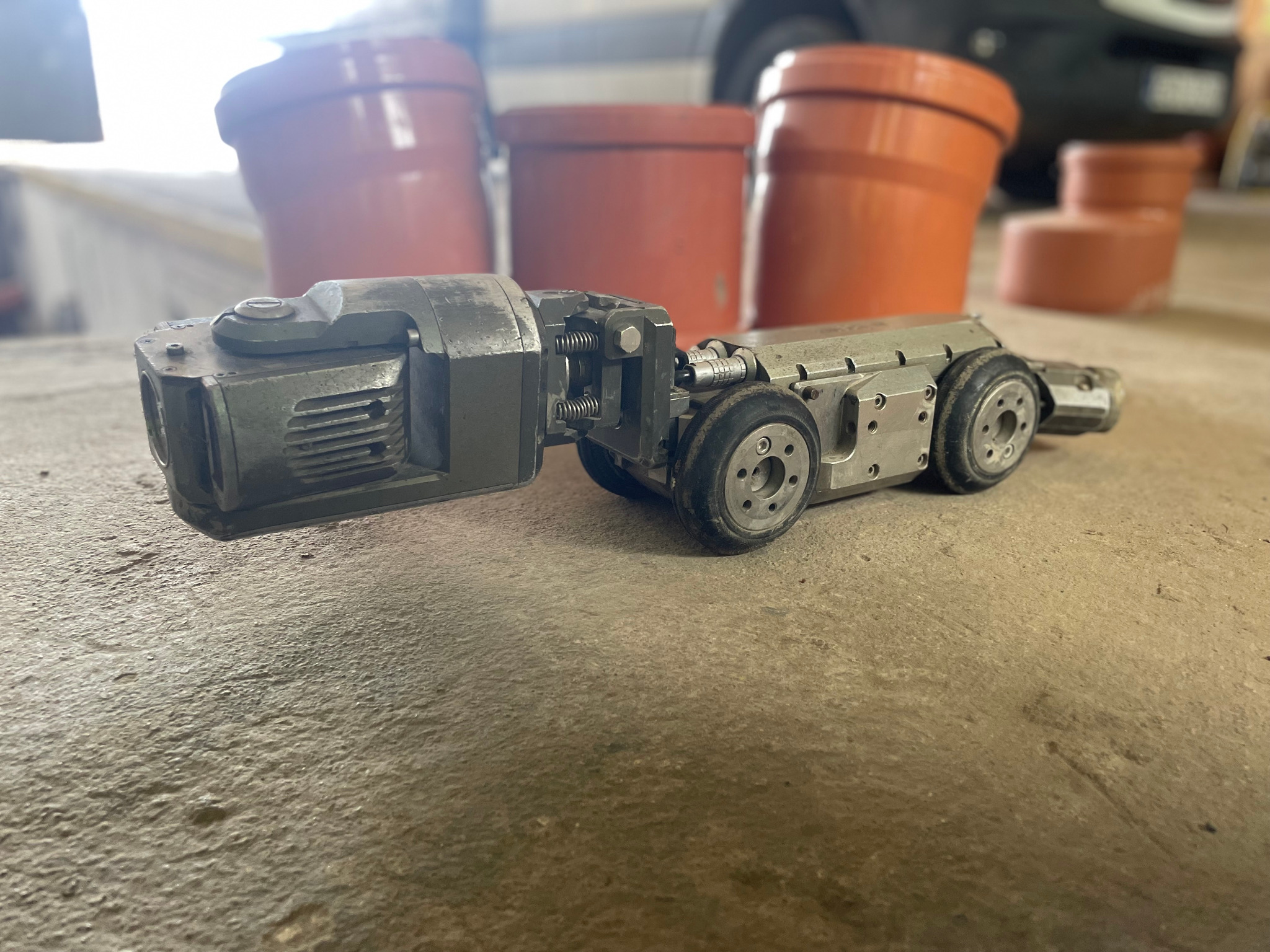 Kamera inspekcyjna na kółkach przed pomarańczowymi rurami kanalizacyjnymi. Detaliczny widok na urządzenie do monitoringu stanu rur.