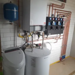 Kompleksowa instalacja grzewcza z kotłem, zbiornikiem, rozdzielaczem i filtrem wody. Miedziane rury na tle białej cegły. Nowoczesne rozwiązanie.