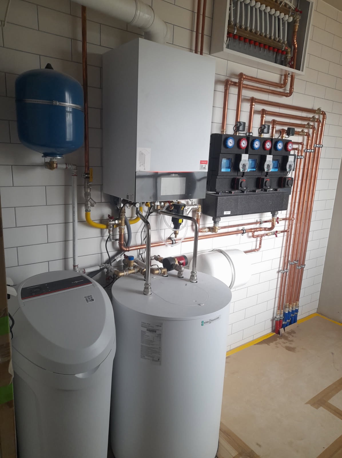 Kompleksowa instalacja grzewcza z kotłem, zbiornikiem, rozdzielaczem i filtrem wody. Miedziane rury na tle białej cegły. Nowoczesne rozwiązanie.