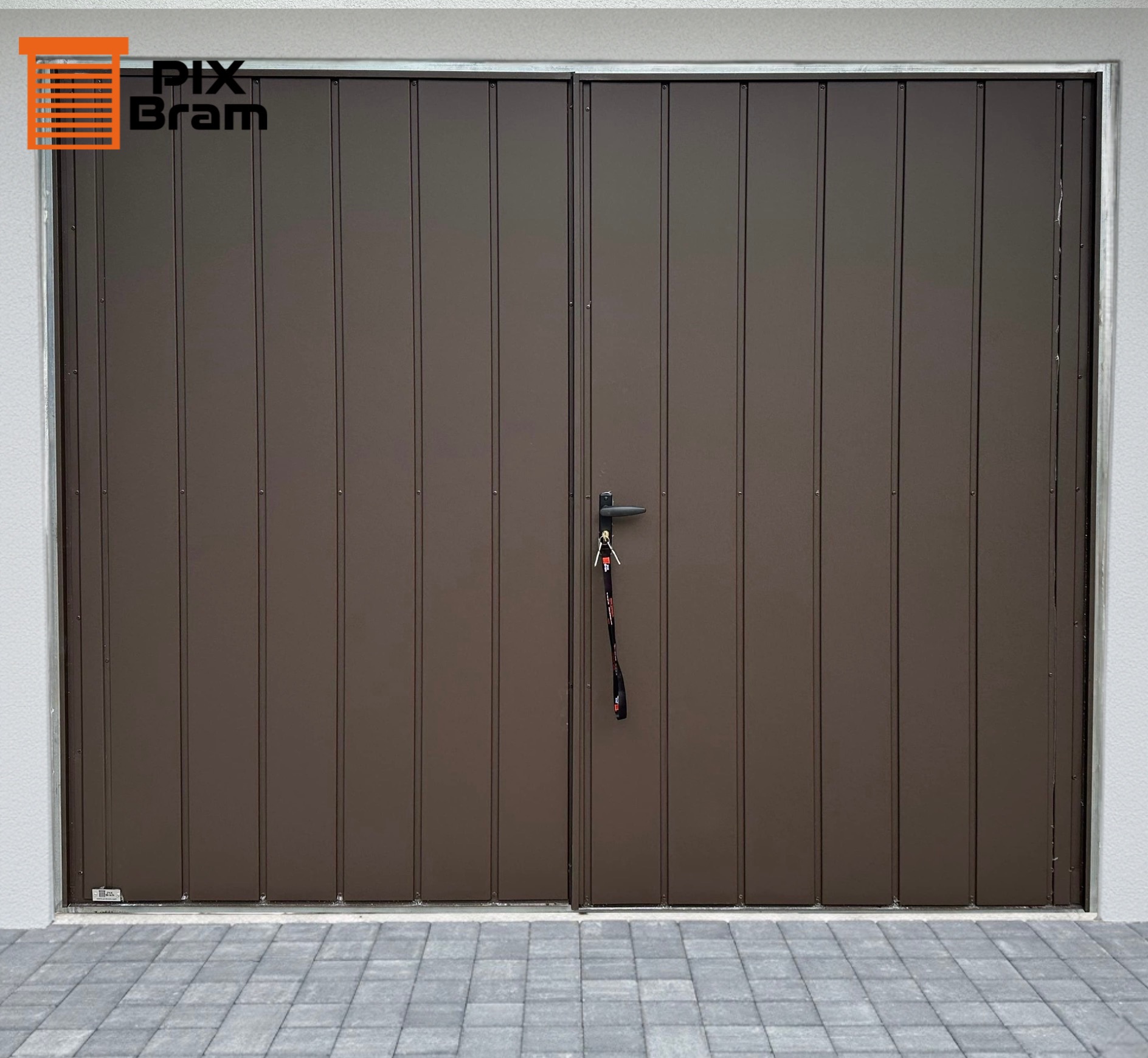 Dwuskrzydłowa, brązowa brama garażowa z pionowymi panelami i czarną klamką, na której wiszą klucze. Widoczna kostka brukowa przed bramą i fragment elewacji.