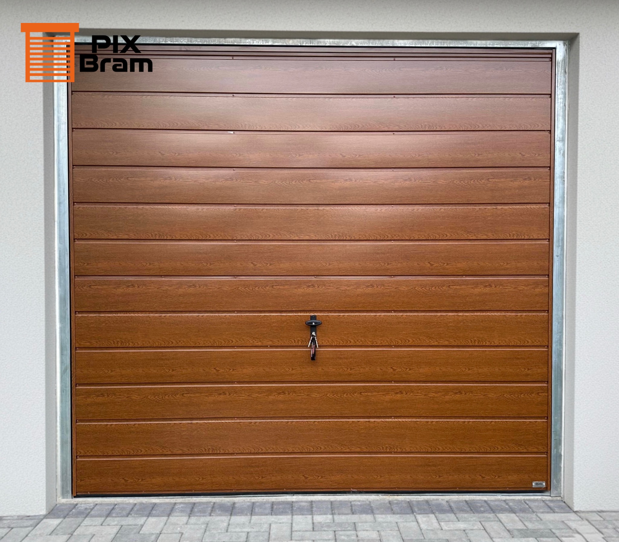 Segmentowa brama garażowa w odcieniach brązu z widocznym zamkiem i kluczem, imitująca drewno, z szarą ramą i fragmentem elewacji.