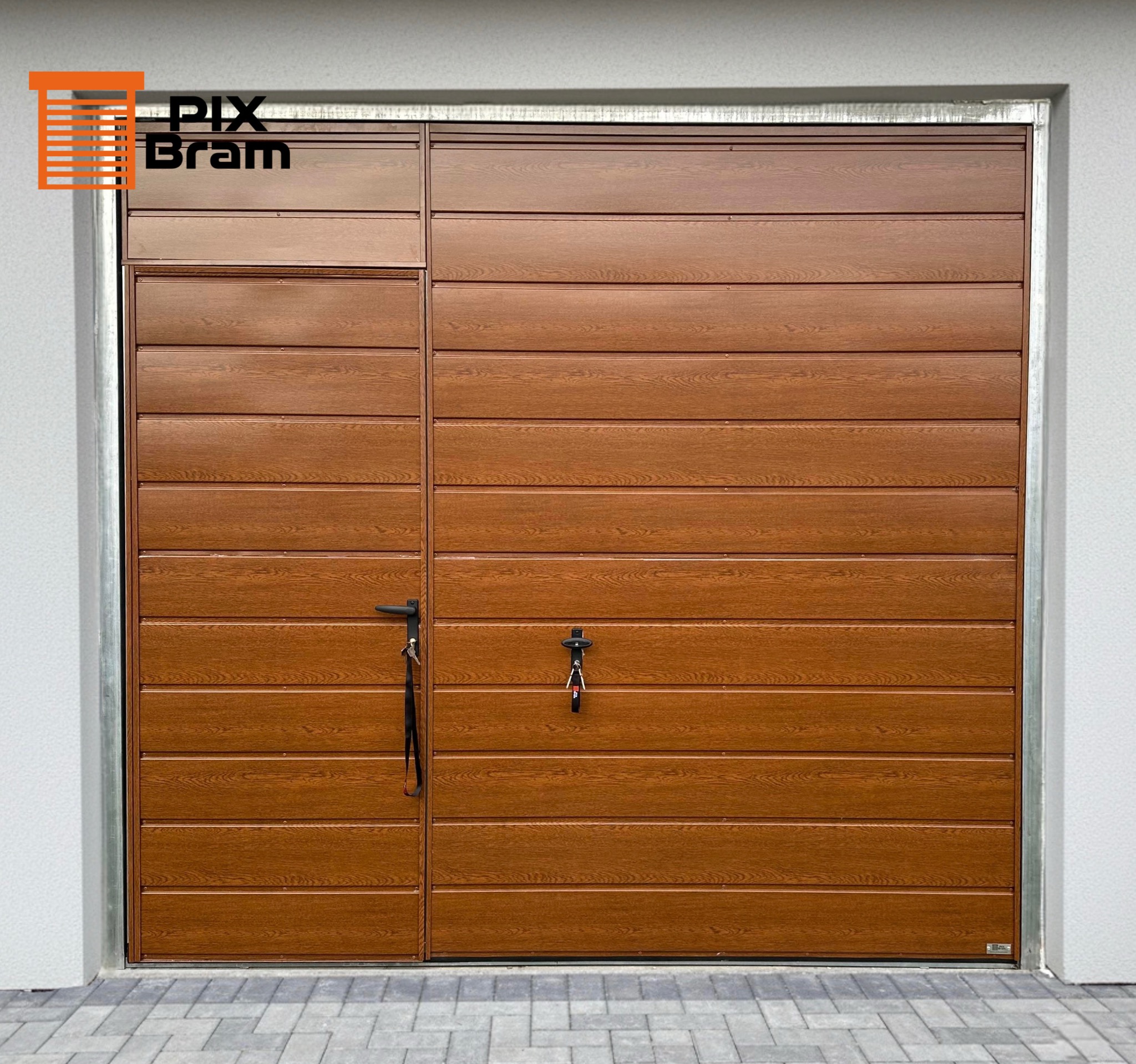 Segmentowa brama garażowa w odcieniach brązu, z poziomymi panelami imitującymi drewno, z czarną klamką i zamkiem, na tle szarej ściany i kostki brukowej.