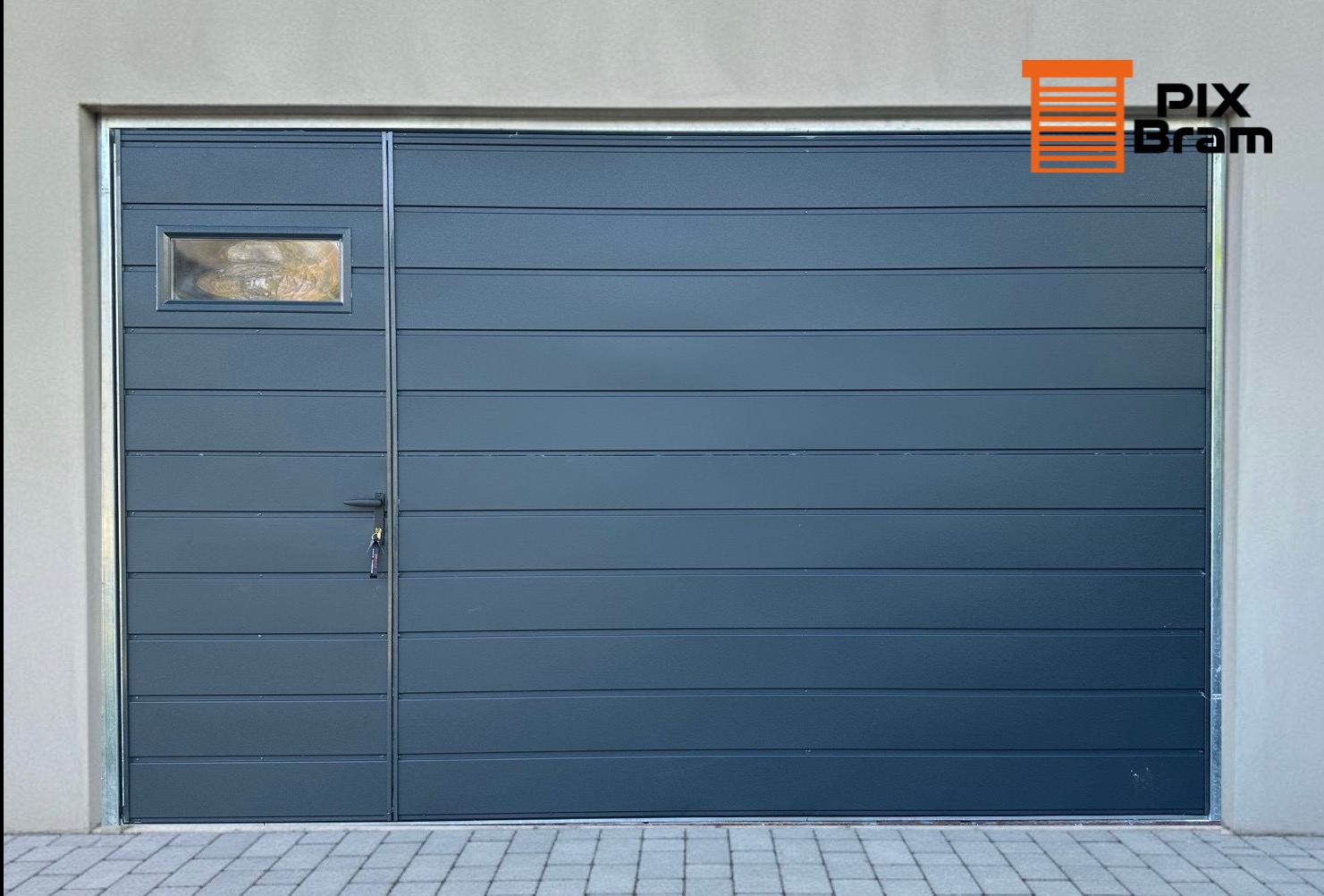 Nowoczesna, segmentowa brama garażowa w kolorze grafitowym z małym oknem i widocznym zamkiem. Brama z poziomymi przetłoczeniami, zamontowana w jasnym budynku.