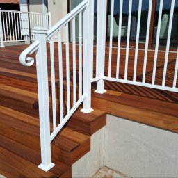 DecorCraft MACIEJ BIŚ - Drewniany taras z białymi balustradami, widok z dołu na schody i fragment tarasu. Ciemne drewno kontrastuje z jasnymi elementami konstrukcyjnymi.