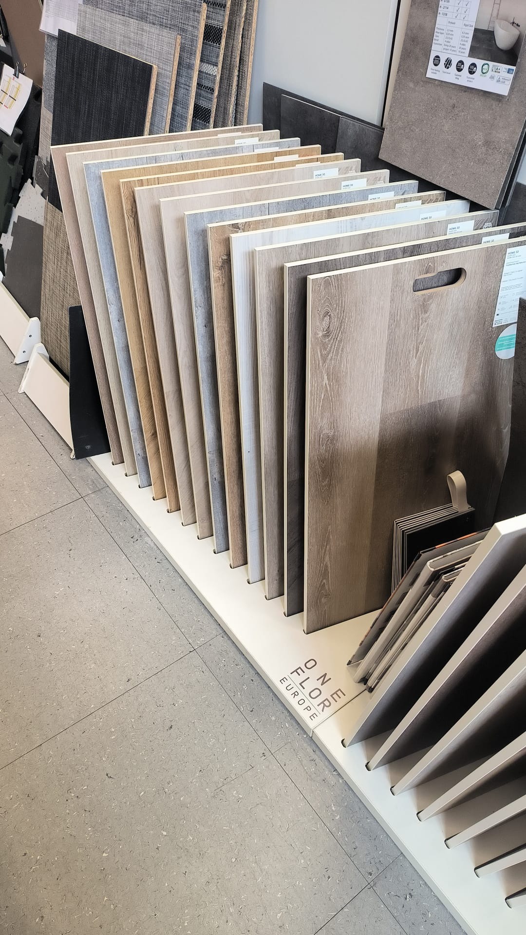 Ekspozycja paneli podłogowych w różnych odcieniach drewna, ustawionych pionowo na białym stojaku z logo 'ONE FLOR EUROPE'.