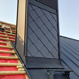 DACHY KOCIEWIE PATRIK PUTTKAMMER - Czarny komin wentylacyjny z romboidalnym wzorem na dachu z blachy na rąbek stojący, widoczne elementy konstrukcji dachu i akcesoria montażowe.