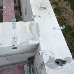 WIKO BOUW Grzegorz Serafin - Wznoszenie ścian z białych bloczków mocowanych metalowymi łącznikami. Widoczne zaprawy i otwory instalacyjne. Ujęcie z góry na budowę.