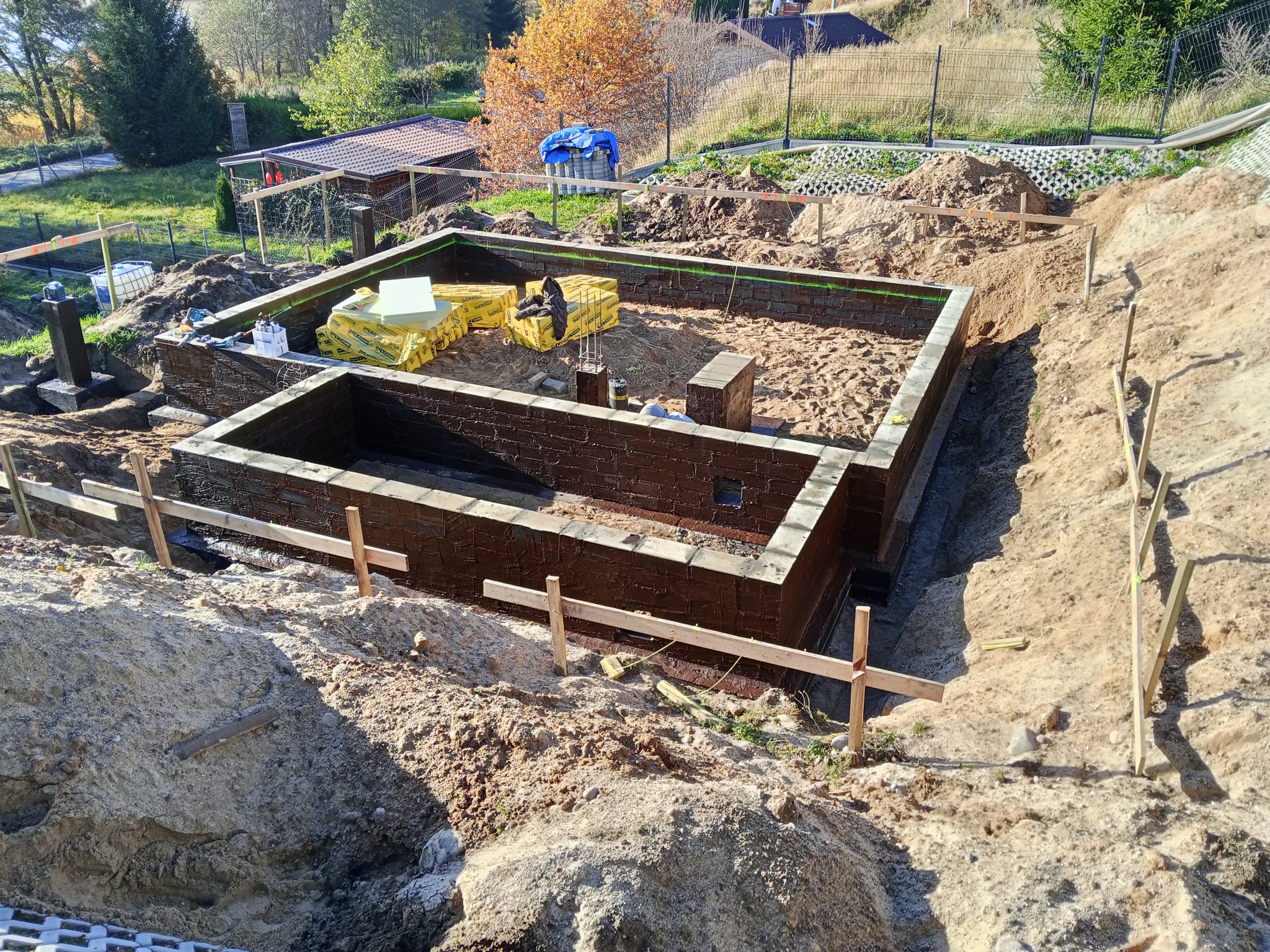 Zabezpieczone fundamenty domu jednorodzinnego, z izolacją termiczną i przeciwwilgociową, przygotowane do dalszych prac budowlanych. Widoczne materiały izolacyjne.