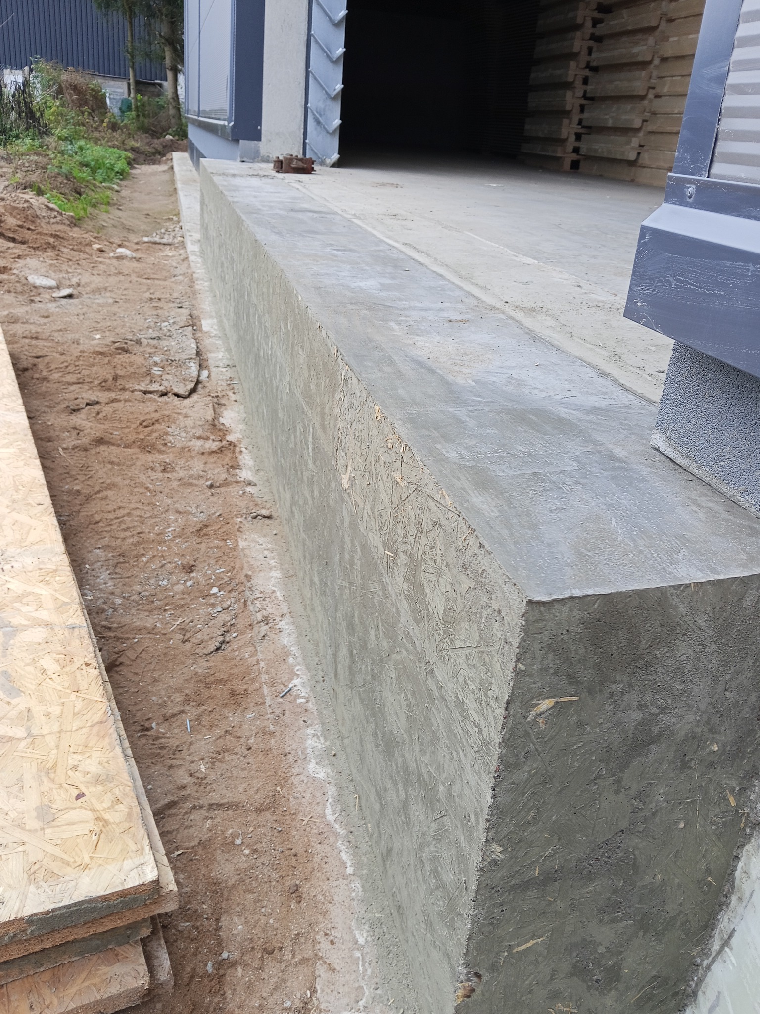 Zabetonowany fundament z widoczną strukturą szalunku z płyty OSB, obok wykop i stos płyt. Widok z góry, lekko z ukosa.