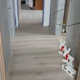 Max Fach Marcin Różek - Wykończony korytarz z panelami podłogowymi i dekoracyjnymi ścianami w odcieniach szarości, widok z perspektywy wejścia. Świąteczne ozdoby na podłodze.