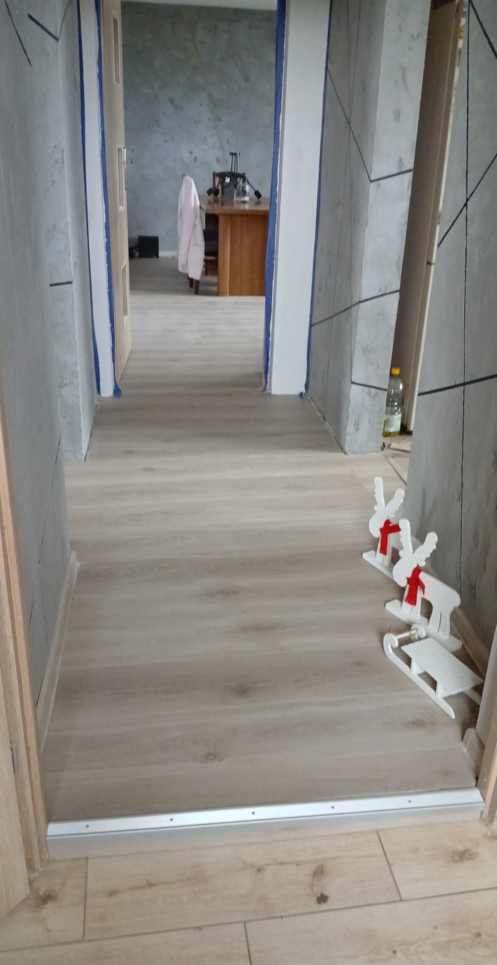 Wykończony korytarz z panelami podłogowymi i dekoracyjnymi ścianami w odcieniach szarości, widok z perspektywy wejścia. Świąteczne ozdoby na podłodze.