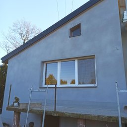 M&M HOUSE - Świeżo otynkowana elewacja domu jednorodzinnego w odcieniach szarości, z widocznymi oknami i elementami rusztowania. Minimalistyczny design, gładka faktura tynku.