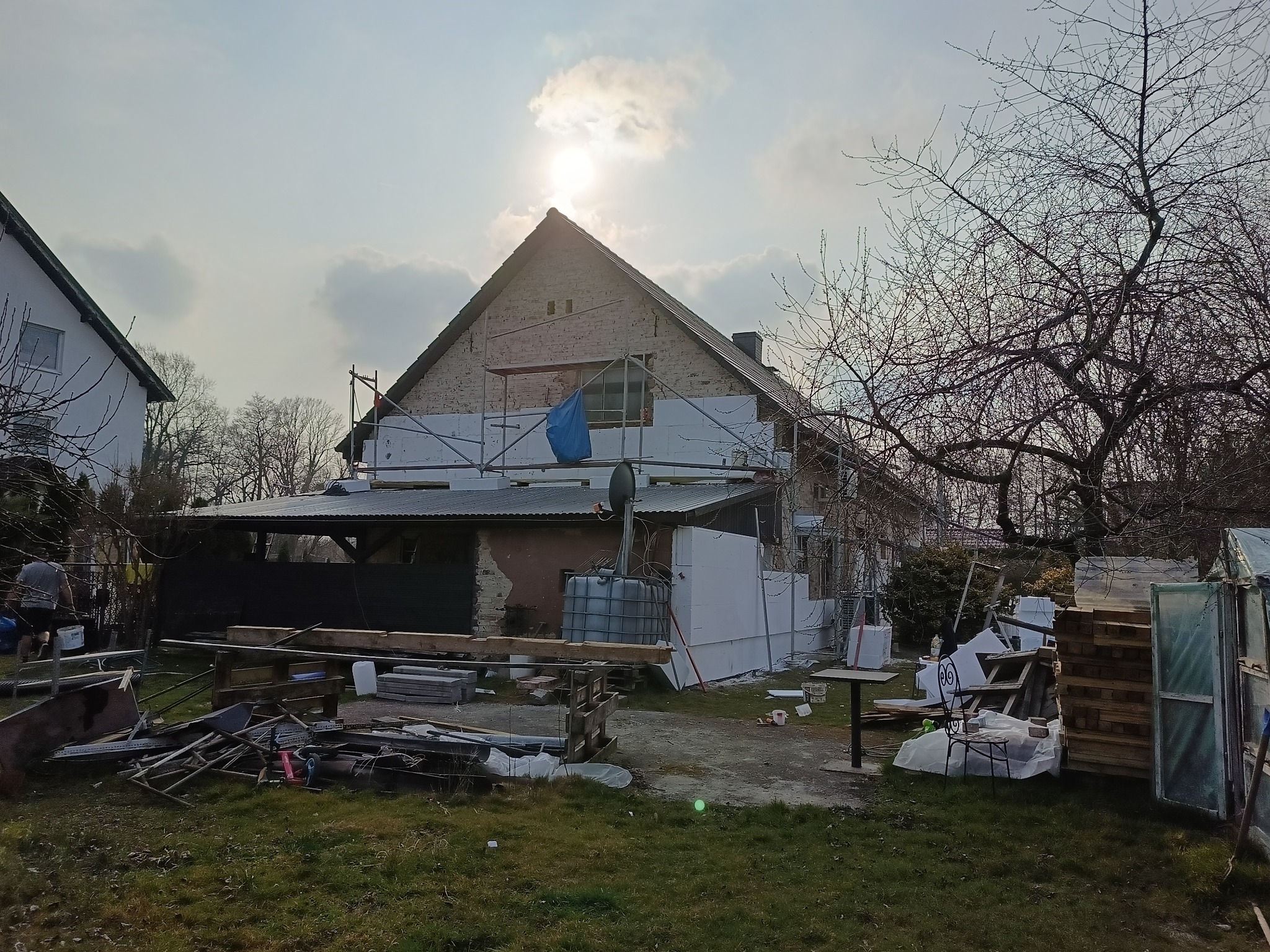 Dom w trakcie ocieplania: biały styropian na elewacji, rusztowania, przygotowane materiały budowlane. Widok na budynek w słoneczny dzień.