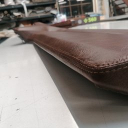 Studio Samochodowe - Brązowy, skórzany element tapicerowany z wyraźnym szwem na blacie roboczym, w tle warsztat tapicerski z półkami i narzędziami.