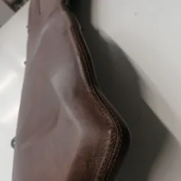 Fragment brązowego, skórzanego siedziska z precyzyjnym szwem, leżącego na jasnej powierzchni. Widoczne detale tekstury skóry i staranne wykończenie.