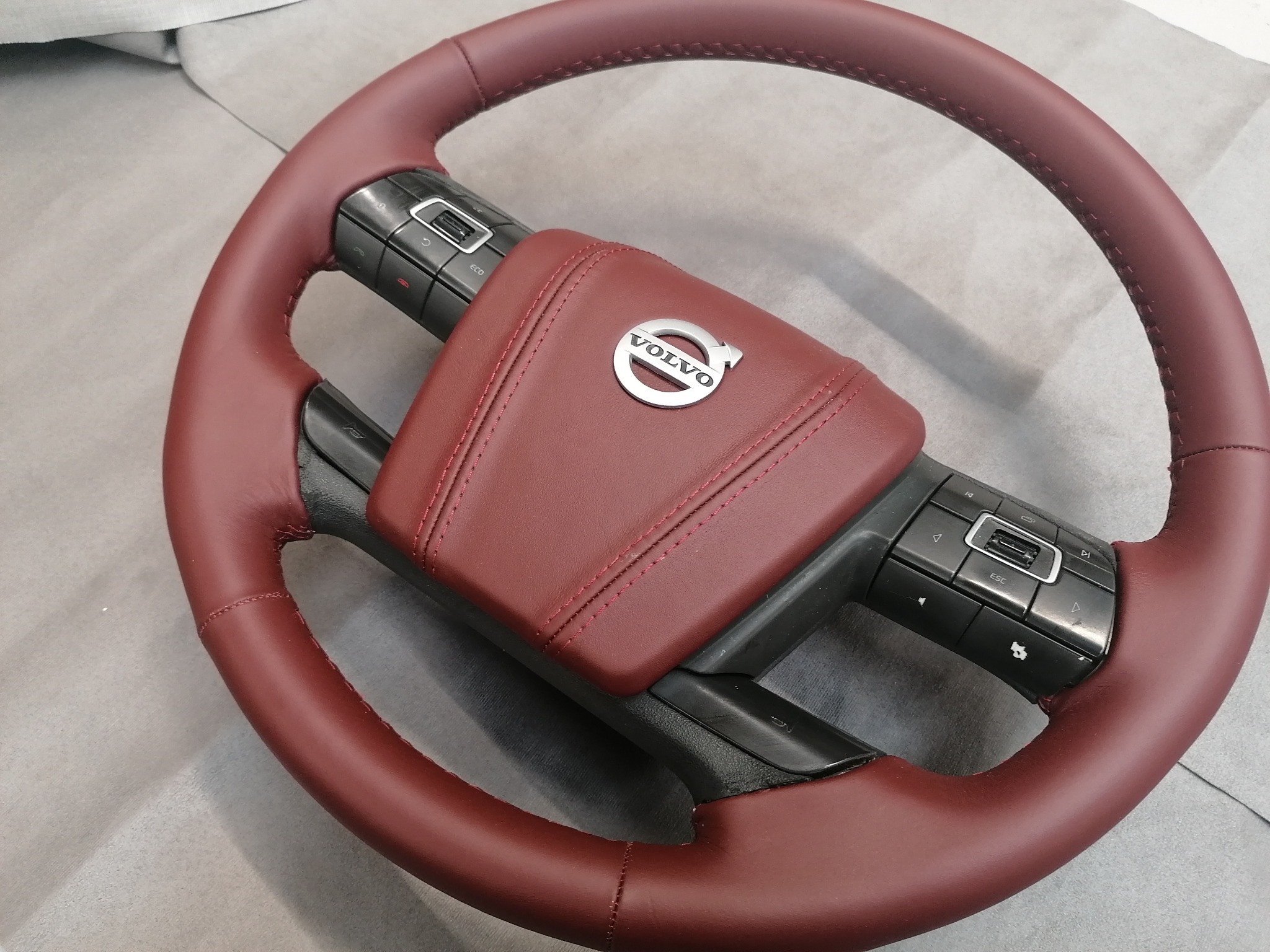 Czerwona, skórzana kierownica Volvo z precyzyjnym szyciem, widoczne przyciski sterowania. Detal tapicerki samochodowej po renowacji.