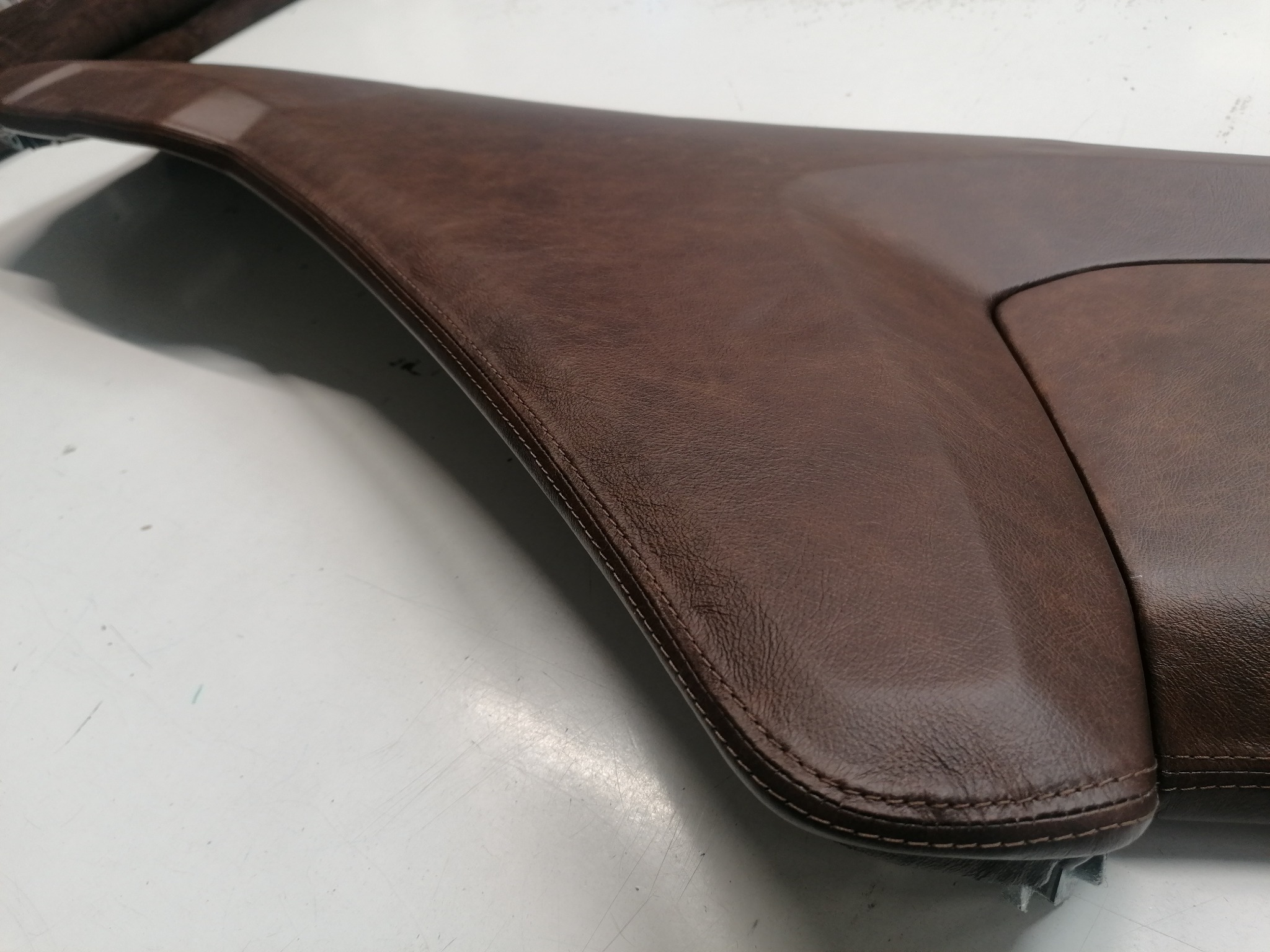 Brązowy, skórzany element deski rozdzielczej auta, po renowacji, z widocznym szwem. Gładka powierzchnia, staranne wykończenie detali, odświeżony wygląd.