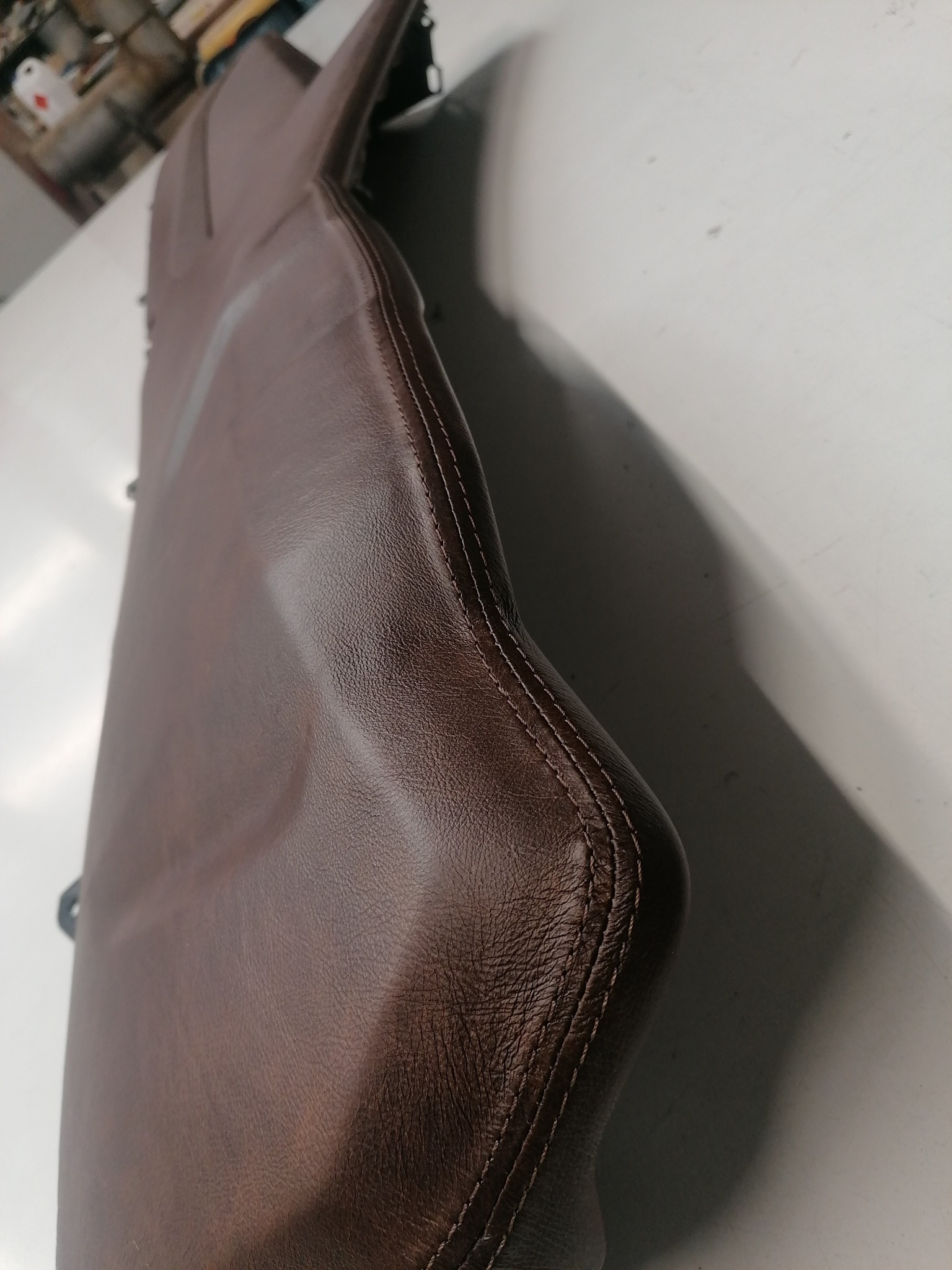 Fragment brązowego, skórzanego siedziska z precyzyjnym szwem, leżącego na jasnej powierzchni. Widoczne detale tekstury skóry i staranne wykończenie.